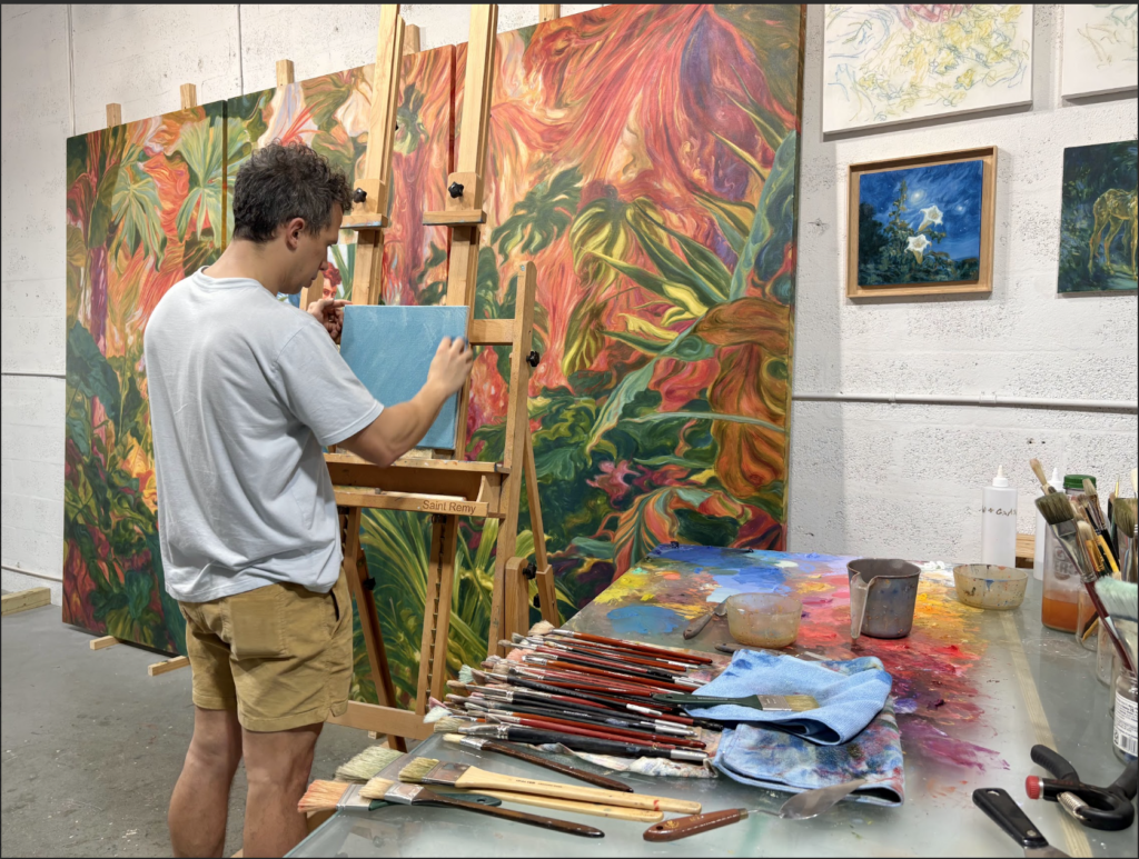 MArlon Portales working in his studio holding a square solid blue canvas and placing it on an easle 